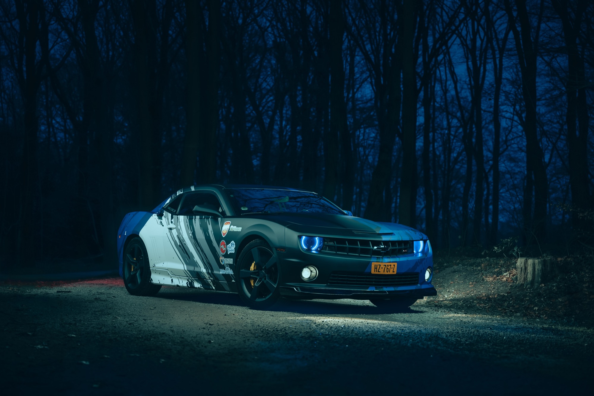 The black-and-blue Camaro 2SS with glowing blue halo headlights in a dark forest