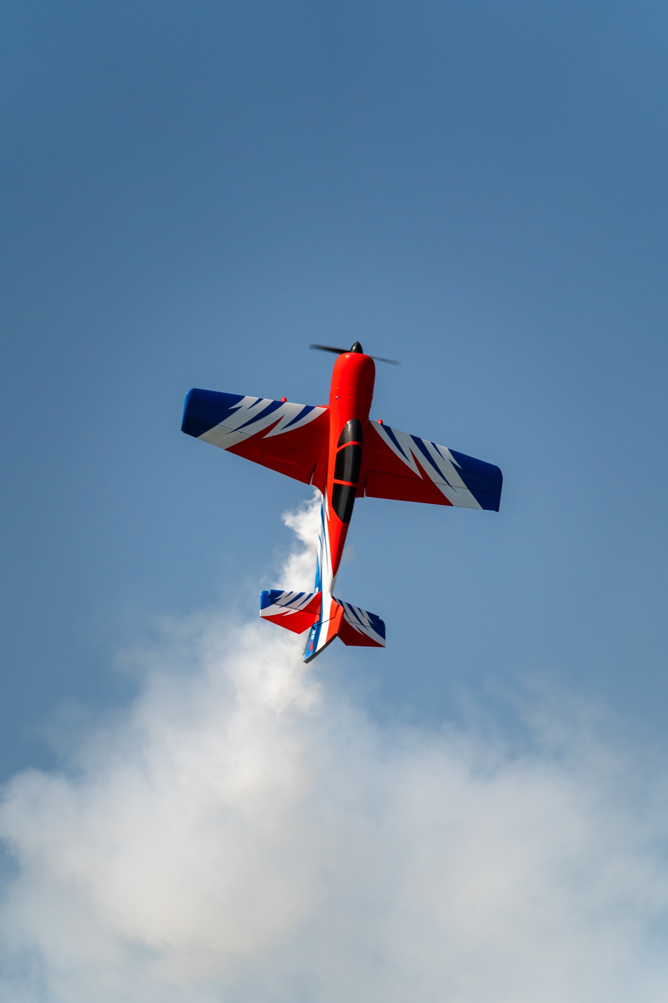 Red aerobatic plane trailing smoke against blue sky