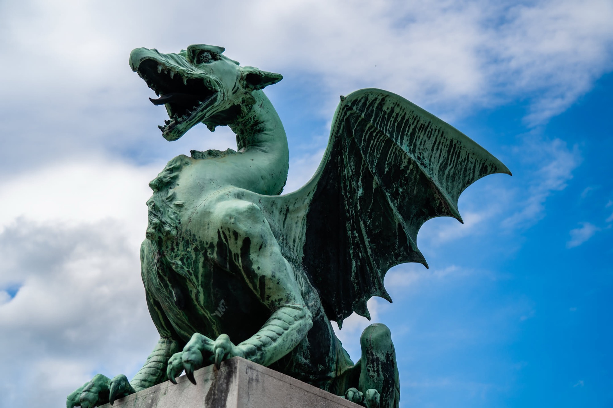 Green bronze dragon statue against a blue sky on the Dragon Bridge in Ljubljana